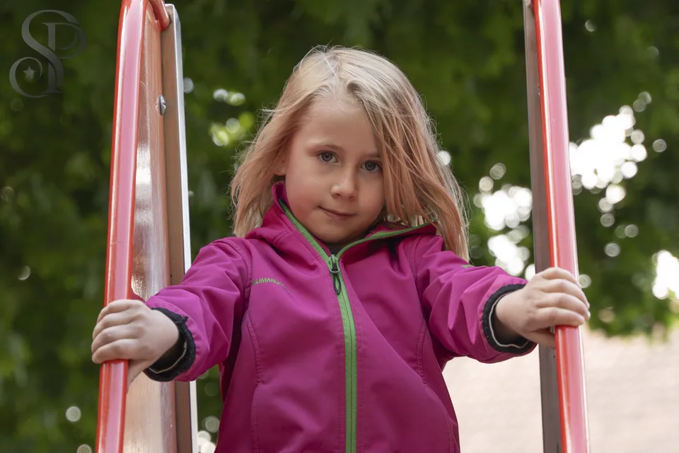 Kind in pinker Jacke zwischen den Griffen einer Rutsche